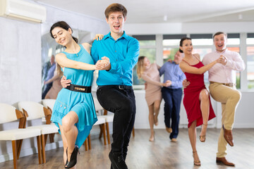 Cheerful young couple enjoying active dancing during group training in dance studio, practicing playful jitterbug movements..