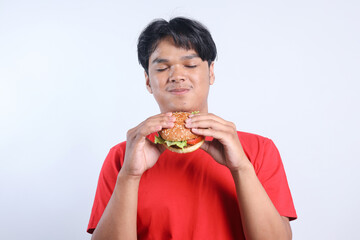 Happy Asian man closed eyes enjoying eating hamburger over white background