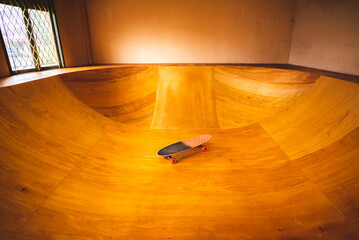 Skateboard on the mini ramp at skate park indoor with brown wooden floor.