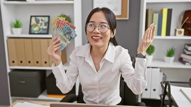 Young chinese woman agape in astonishment at office, clutching australia dollars; a picture of disbelief on her scared face