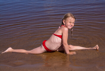 Fototapeta na wymiar A girl plays on a sandy beach on the shore of a lake in the summer heat.