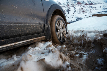 The side view of a car reveals the vehicle's wheel deeply embedded in snowy terrain, hinting at the...