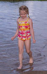 A girl plays on a sandy beach on the shore of a lake in the summer heat.