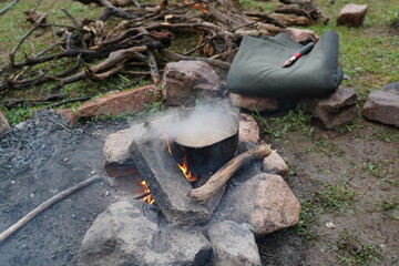  A pot bubbles over a campfire, surrounded by a woodpile and camping gear. The scene captures the essence of outdoor living and wilderness survival.
