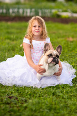 On a hot summer day outside, a beautiful, elegant girl is holding a French bulldog in her arms. A model girl and a dog.