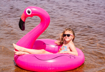 On a hot summer day, a child is relaxing on the lake. A girl on the beach. A girl swims on an inflatable pink flamingo.