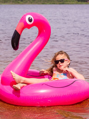 On a hot summer day, a child is relaxing on the lake. A girl on the beach. A girl swims on an inflatable pink flamingo.