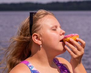 On a hot summer day, a child is relaxing on the lake. A girl on the beach. The girl is holding a pink donut in her hands.