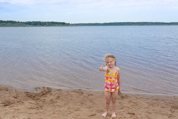 A girl plays on a sandy beach on the shore of a lake in the summer heat.