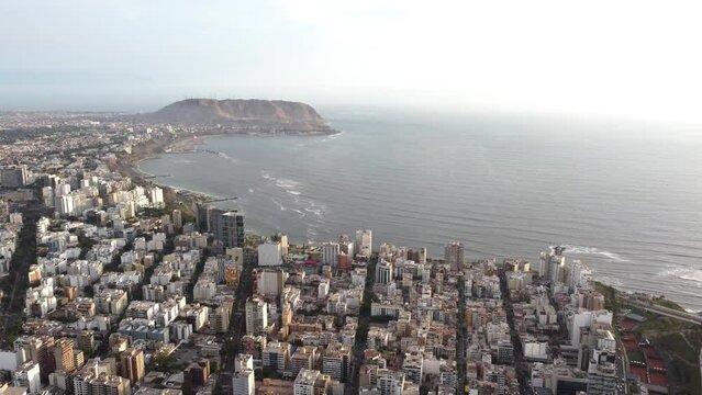Drone shot of a dense, urban coastline as the evening light casts shadows over the landscape in Lima - Peru