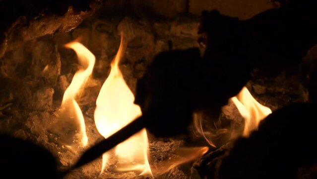 Skewered meat sizzles as it is grilled over crackling flames in a fireplace. Traditional Mtsvadi preparation over an open fire at night, close-up view.