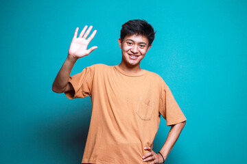 Young Asian man waving hand saying hello goodbye on blue background