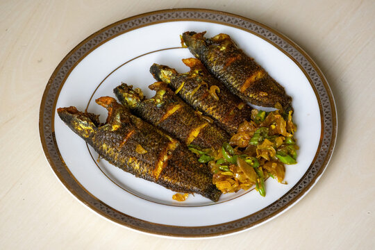 Delicious fried koi fish garnished with chopped onions and green chillies on a plate. The scientific name of this fish is Anabas testudineus, commonly known as the climbing perch.