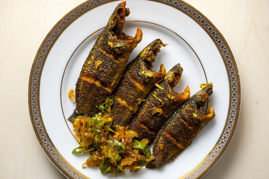 Delicious fried koi fish garnished with chopped onions and green chillies on a plate. The scientific name of this fish is Anabas testudineus, commonly known as the climbing perch. Top view.