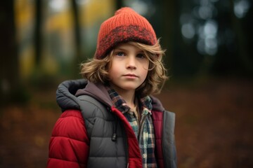 Portrait of a little boy in a red cap and coat in autumn forest