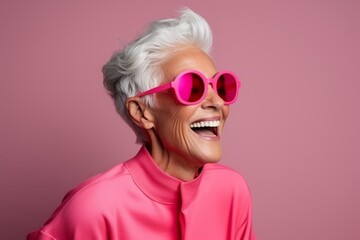 Portrait of a happy senior woman with pink sunglasses over pink background