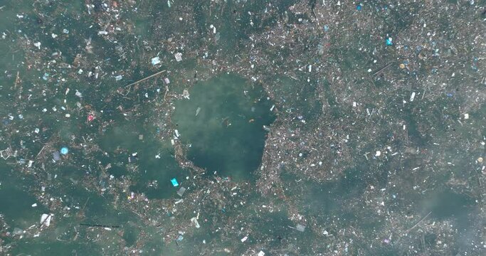 Top down quickly ascending drone shot of polluted water filled with trash floating over dead coral reef in the turqouise tropical water of  Bali Indonesia
