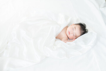 シーツに包まれて眠る生後4ヶ月の男の子