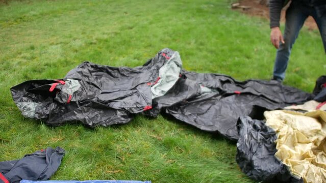 A man laying out a tent on the ground at a campsite before pitching it.