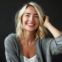 Portrait of a happy blonde woman in a gray cardigan, joyfully laughing showing her teeth against a dark backdrop