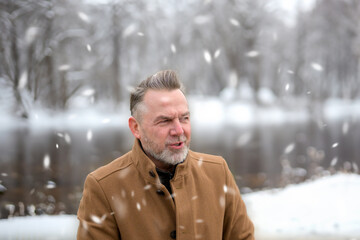Middle-aged man in front of a snowy winter landscape while it is snowing