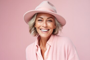 Portrait of smiling senior woman in pink hat over pink background.