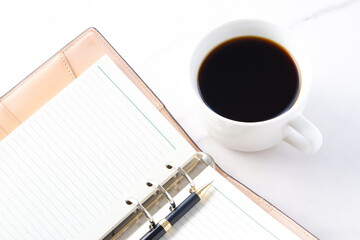 淹れたてのコーヒーを飲みながら、リング式のシステム手帳を開いてデスクワークをしているイメージ
