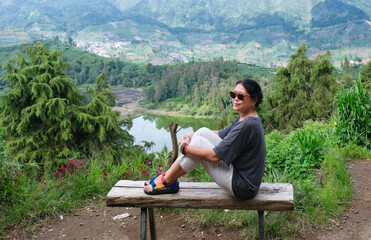 Woman enjoying fresh air sitting on a bench over hilltop with beautiful nature in the background