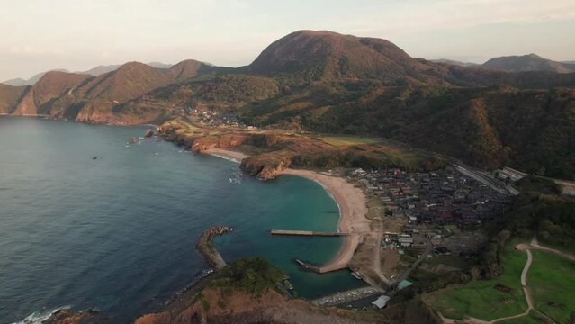 Aerial drone landscape of japanese blue sea bay in kyoto kyotango island summer coastline, white sand beach with nearby village, Japan during daylight, mountain range background