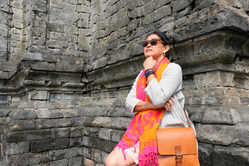 Asian woman leaning on old stone wall of Bima Temple in Dieng, Wonosobo