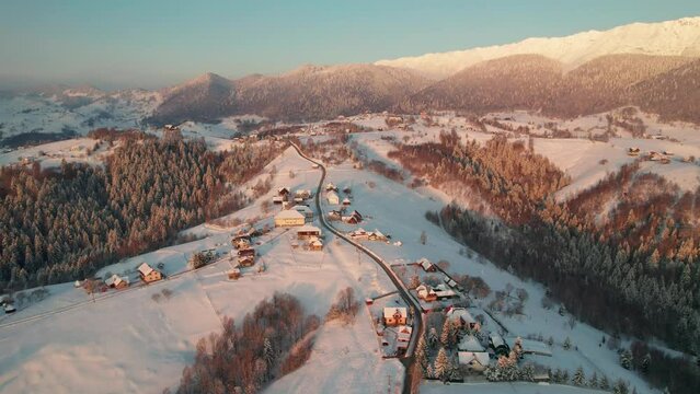 Sunrise glows over Pestera Village with snow-covered roofs, aerial winter wonderland
