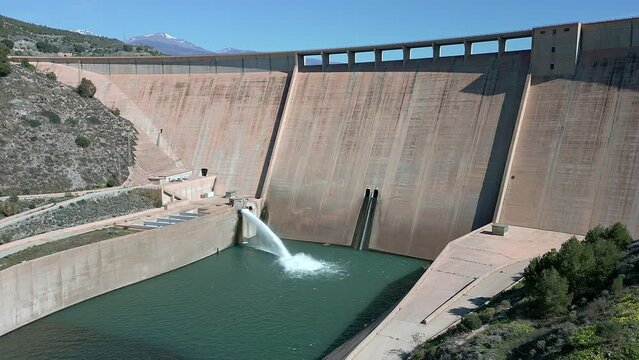 Gravity dam discharging water. Howell bunger valve in operation.  Descending aerial view over the dam and river. Renewable energies. Hydroelectric satation.