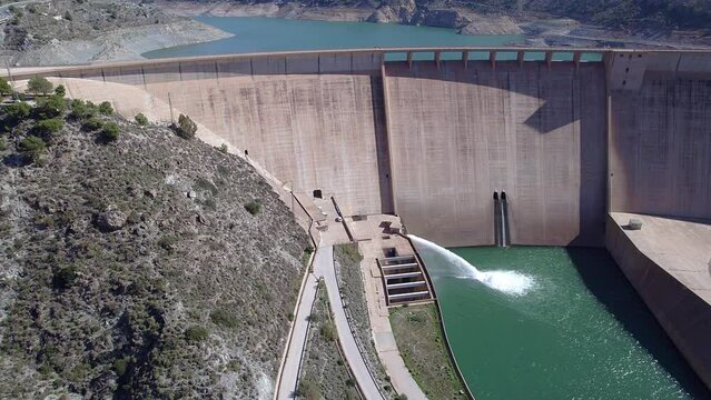 Gravity dam discharging water into the river. Howell bunger valve in operation.  Orbit aerial view over the dam and river. Renewable energies. Hydroelectric satation.