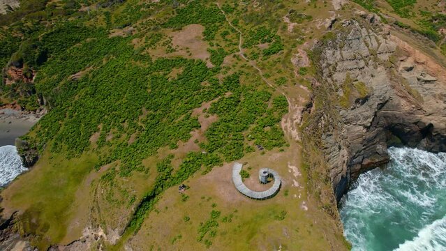 Aerial wide view of Muelle del Tiempo, spiral wooden structure at Sea shore cliff, Cucao, Tepuhueico park