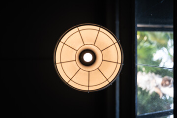 A classic style round ceiling lamp with glowing lightbulb in warm light shade, with dark area as...