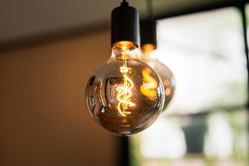 Classic lighting bulbs are glowing in orange warming shade, there are hanging from ceiling for Interior cozy style decoration. Close-up and selective focus.