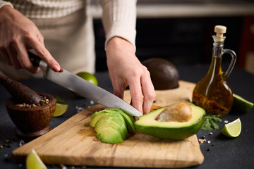 Salsa recipe - Woman Cutting slicing fresh green avocado fruit with knife on a wooden board at domestic kitchen