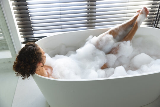 Woman relaxes in a bubble bath at home, legs playfully raised
