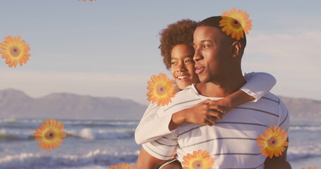 Image of flowers over happy african american father with son on sunny beach
