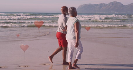 Image of hearts over senior african american couple walking on sunny beach