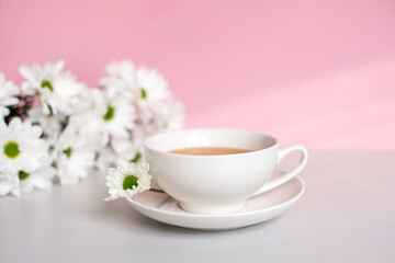 White set cup with a plate for tea and coffee stand on a pink background with chamomile flowers