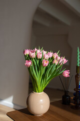 Pink tulips in a beige vase on a wooden table