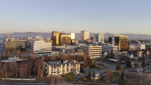 HDR stock drone video of Anchorage city skyline at sunset with warm glow on buildings. Aerial view of Alaskan city moving up and left