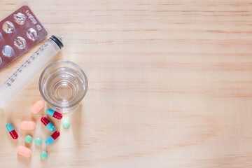 Close up pills and tablets with glass water on wooden table.