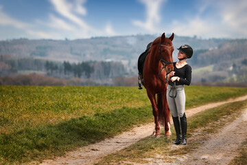 Rider and horse stand side by side on a path in a wide spring landscape.