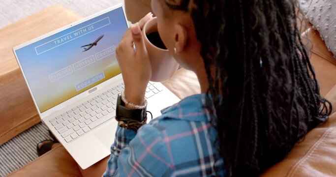 A young African American woman is booking a trip online using her laptop on the couch at home