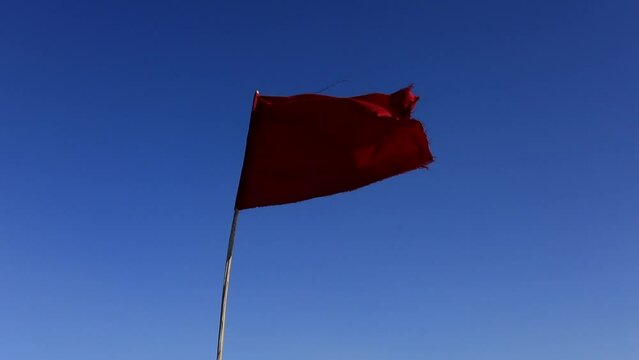 Red flag fluttering against clear blue sky in Tunisian salt desert, Chott el Jerid, symbol of caution