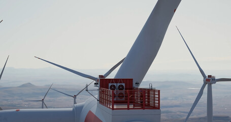 Large wind turbine rotating blades . Engineer performing repairing and maintenance works on top of wind turbine nacelle house.
