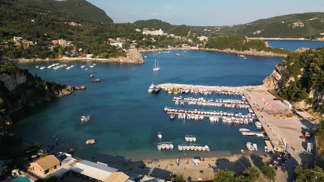 Aerial pullback above bustling harbor and sandy beach in Corfu Greece with coastal view homes and shops