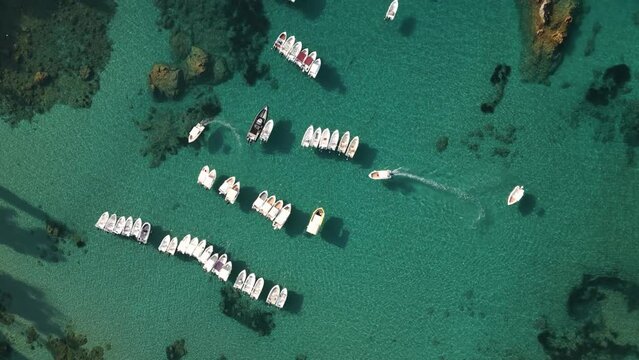 Top down overview of small skiff boat turning to anchor in row by other similar marine vessels in Corfu Greece